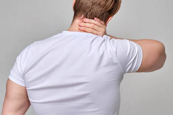 Um homem com uma t-shirt branca massaja o pescoço com dores. Conceito de surto de trabalho . — Fotografia de Stock