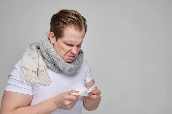 A man with a white T-shirt blew his nose in a handkerchief. The concept of the disease of the common cold, flu. — Stockfoto