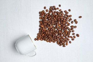 An abstract fountain of coffee beans made from a white cup on a wooden background.