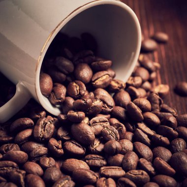Square format. Coffee beans fall out of the white cup. Toned.