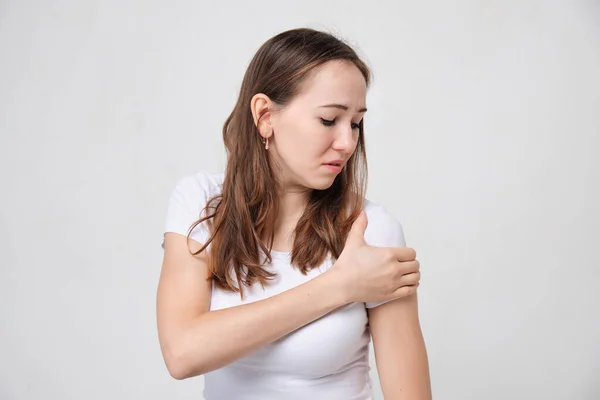 A girl in a white T-shirt massages her shoulder in pain. — Stockfoto