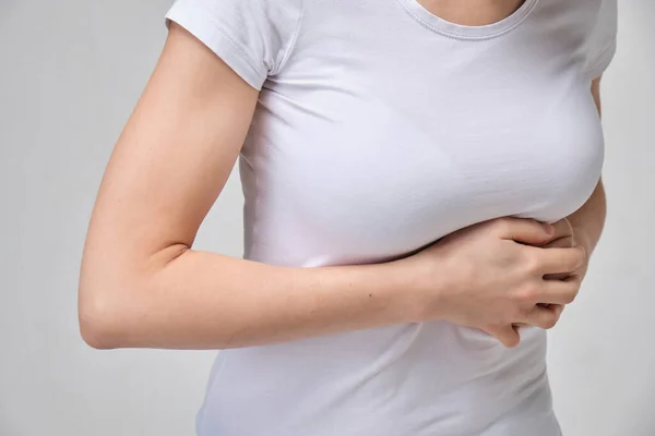 A girl in a white T-shirt is massaging under her breasts. The concept of intercostal neuralgia.
