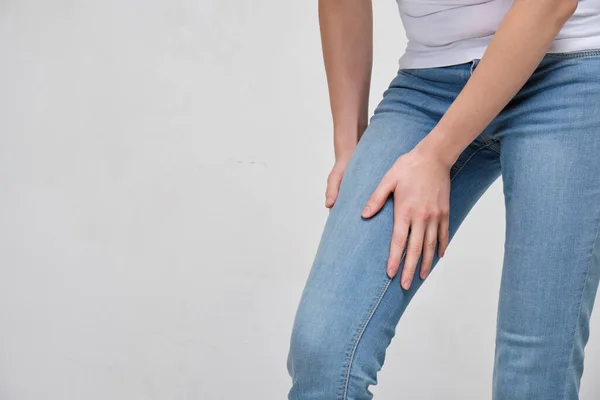 Una chica con una camiseta blanca y jeans se está masajeando el muslo. Conduce el músculo . — Foto de Stock