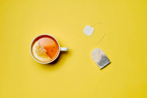Il concetto di preparare il tè da una bustina di tè. Una tazza di tè con limone su sfondo giallo . — Foto Stock