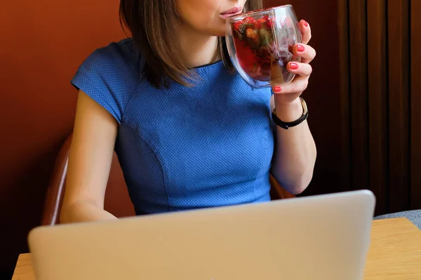 Κορίτσι σε ένα καφέ πίνει νόστιμο τσάι με μούρα, ενώ εργάζονται σε ένα φορητό υπολογιστή. — Φωτογραφία Αρχείου