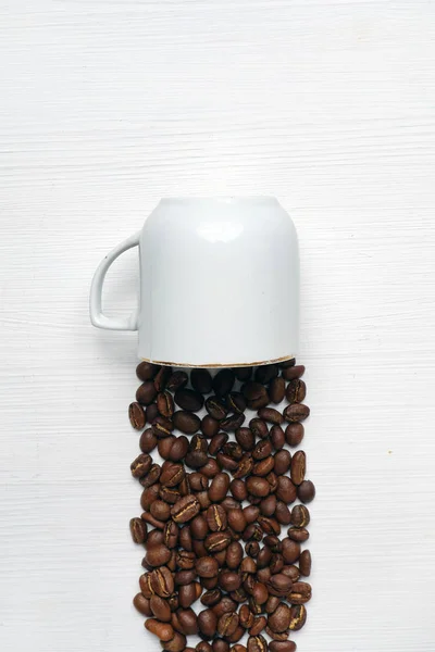 El café abstracto de los granos, que es vertido de la taza blanca sobre el fondo blanco de madera . — Foto de Stock