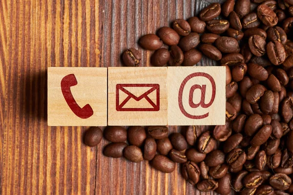 Abstract contact icons - phone, envelope, e-mail on coffee beans on the burnt background.