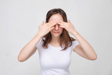 A girl in a white T-shirt massages her eyelids. The concept of severe pain in front of the head.