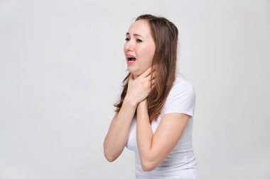 A girl in a white T-shirt holds his throat. The concept of suffocation, asthma, pant.