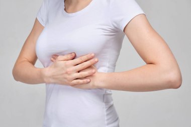A girl in a white T-shirt massages her chest. Breast problems.