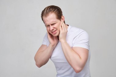 A guy in a white T-shirt massages his ears - terrible pain due to inflammation.