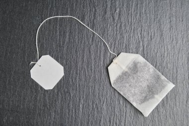 A tea bag with a white label for mock, copy space on the black slate. Top view.