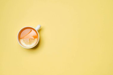 A cup of tea with lemon on a yellow paper background. Top view.