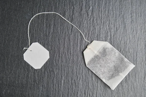 A tea bag with a white label for mock, copy space on the black slate. Top view. — Stock Photo, Image