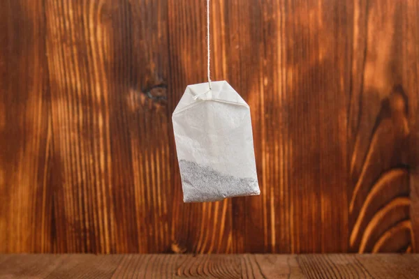 A packet of tea hangs in the air on a burnt wooden background. — Stok fotoğraf