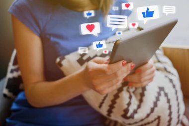 A girl dressed in a blue dress communicates on social networks through a tablet. Abstract icons of likes, hearts, thumbs up, messages.