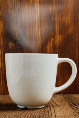 A hot cup of tea with steam over it against a burnt wooden background.