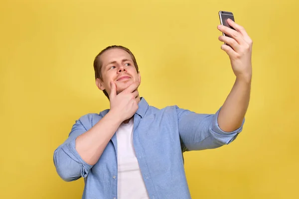 Ein Mann im blauen Hemd auf gelbem Hintergrund macht ein Selfie auf einem Smartphone für soziale Netzwerke. — Stockfoto