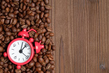 Yanmış ahşap zemin üzerinde kırmızı analog saat bulunan dağınık kahve çekirdekleri. Uzayı kopyala Üst görünüm.