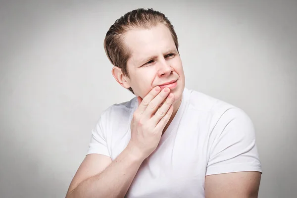 En man i vit t-shirt masserar käken av smärta efter att ha dragit ut en tand. Tonad. — Stockfoto