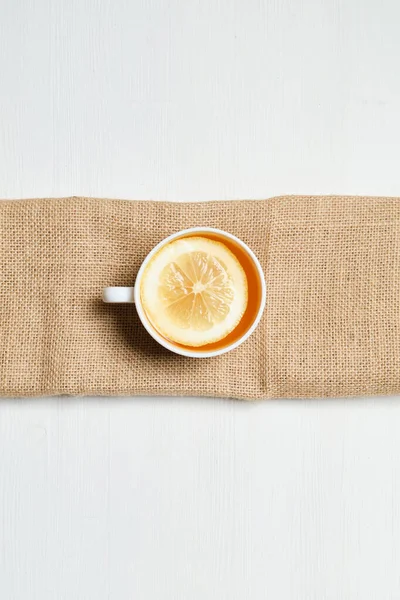 Cup of tea on a knitted rag and white wooden background. Top view. Vertical. — Stock Photo, Image