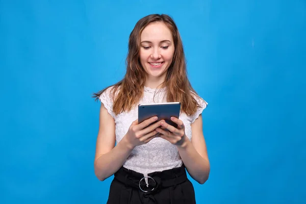 Brunette girl in casual clothes on a blue background and watching funny films, TV shows, shows through a tablet — 图库照片