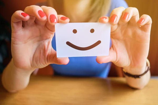 Girl works holding a piece of paper with a smiley face. The concept of a good mood. — Stockfoto