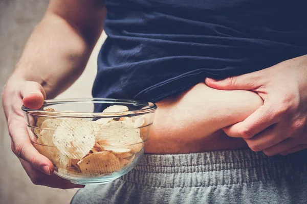 The man abstractly shows obesity and holds a glass plate with chips. — Stockfoto