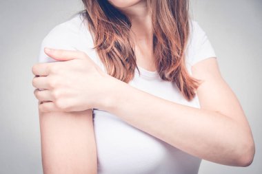 A girl in a white T-shirt massages her shoulder after an injection. Toned.