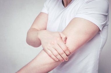 A man in a white T-shirt suffers from pain after the gym in the elbow joint. Toned.