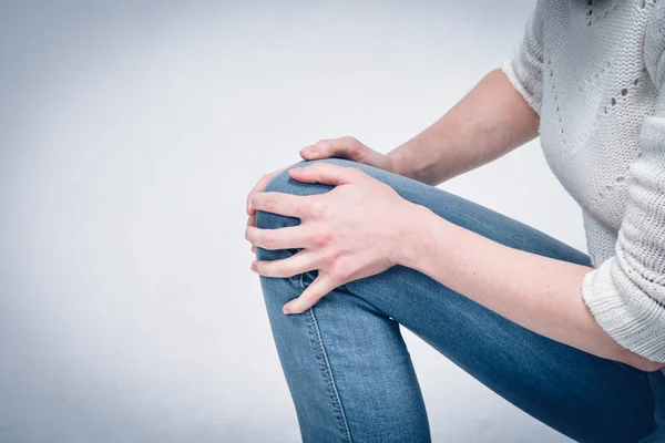 Девушка в белом свитере и джинсах массирует колено после сильного синяка на земле . — стоковое фото