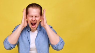 A man in a blue shirt on a yellow background screams strongly and hands near his head. The concept of crazy discounts on sale.