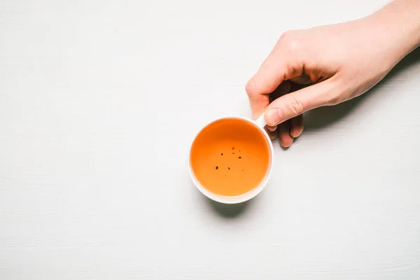 Man hand holds a mug with tea on a white wooden background with copy space. Top view. — 스톡 사진
