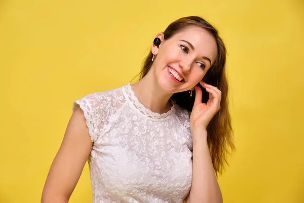 Chica en una camiseta sobre un fondo amarillo lleva auriculares inalámbricos. El concepto de transición a las nuevas tecnologías . —  Fotos de Stock