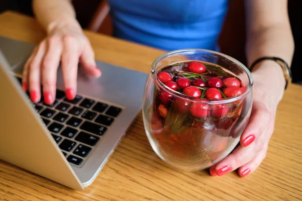 A girl in a blue dress sits at a cafe, relaxes watching movies, TV shows on a laptop and drinks delicious tea with red berries. — Φωτογραφία Αρχείου
