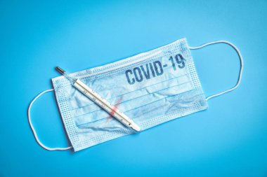 Koruyucu maskenin üzerindeki yazı mavi arka planda 39 derece sıcaklık gösteren termometrenin yanındaki Coronavirus Covid-19. Salgın hastalık konsepti. Kapat..