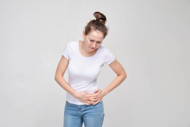 Beyaz tişörtlü ve kot pantolonlu bir kız vücudunun sol tarafına acı içinde masaj yapıyor. Kapat..