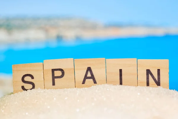 ビーチのぼやけた写真と抽象的な砂の中の木製のブロックに単語のスペイン語 最も人気のあるリゾートの1つ — ストック写真