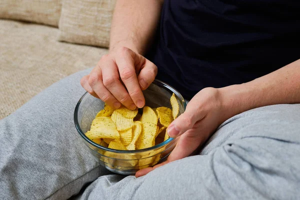 A man is resting eating potato chips from a glass dish. Close up.