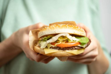 Kız elleriyle bir hamburger tutuyor. Kapat..