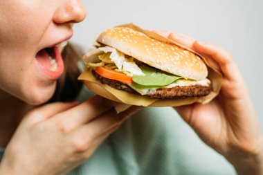 Kız elleriyle bir hamburger tutuyor ve onu iştahla yiyor. Kapat..