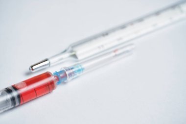 Beyaz arka planda termometrenin yanında ısıyı düşürmek için kırmızı şırınga. Kapat..