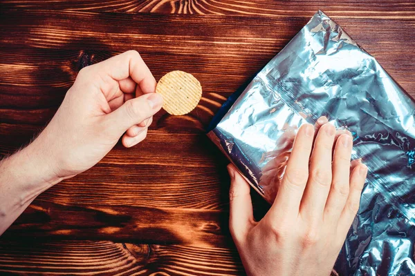 Handen Nemen Een Chip Uit Folie Verpakking Een Houten Achtergrond — Stockfoto