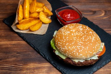 Köy patatesli ve ketçaplı hamburgerler ve tahta üzerine siyah tahta ve yanmış ahşap arka plan. Kapat..