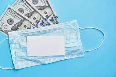 Mavi arka planda 100 dolarlık tıbbi maske. Kapatın. Kopyalama alanı için beyaz kart.