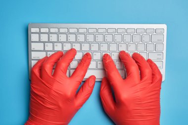 Kırmızı eldivenli doktor mavi arka planda bir klavyeye yazı yazıyor. Üst görünüm.