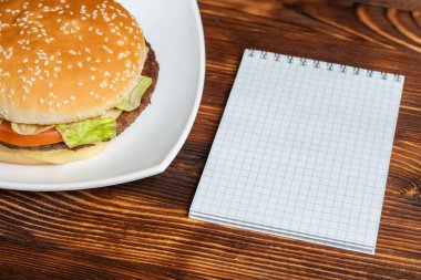 Beyaz tabakta hamburger ve defterli ahşap bir arka plan. Kapat..