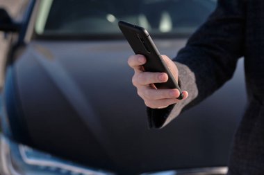 Ceketli bir adam arabanın arka planında akıllı telefon tutuyor. Kapat..