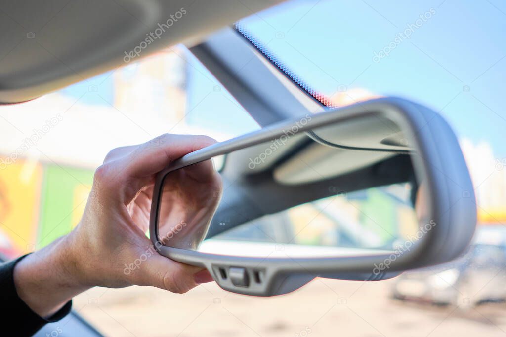 A man in a modern car. Hand adjusts the rearview mirror. Close up.