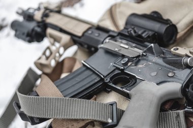Bir saldırı tüfeği askeri bir evrak çantasının üzerinde duruyor. Kapat..